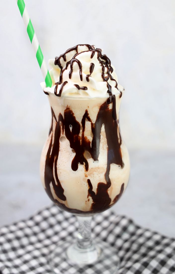 Bailey's Milkshake topped with whipped topping and chocolate syrup on a gray plaid napkin on a concrete backdrop