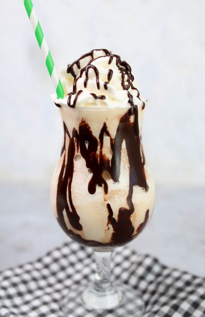 Bailey's Milkshake topped with whipped topping and chocolate syrup on a gray plaid napkin on a concrete backdrop