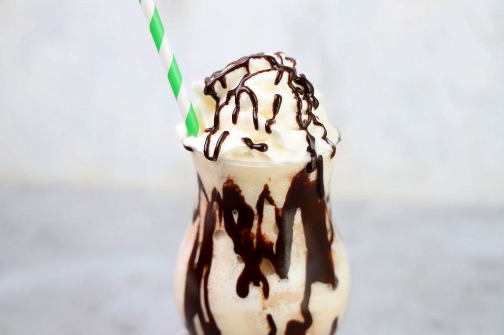 Bailey's Milkshake topped with whipped topping and chocolate syrup on a gray plaid napkin on a concrete backdrop