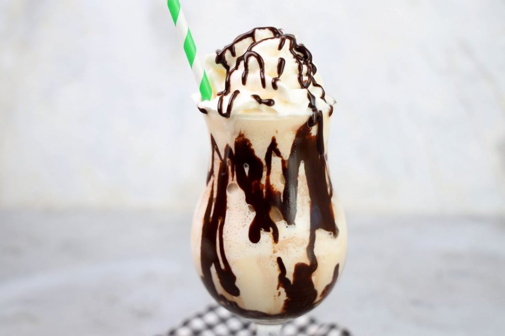 Bailey's Milkshake topped with whipped topping and chocolate syrup on a gray plaid napkin on a concrete backdrop