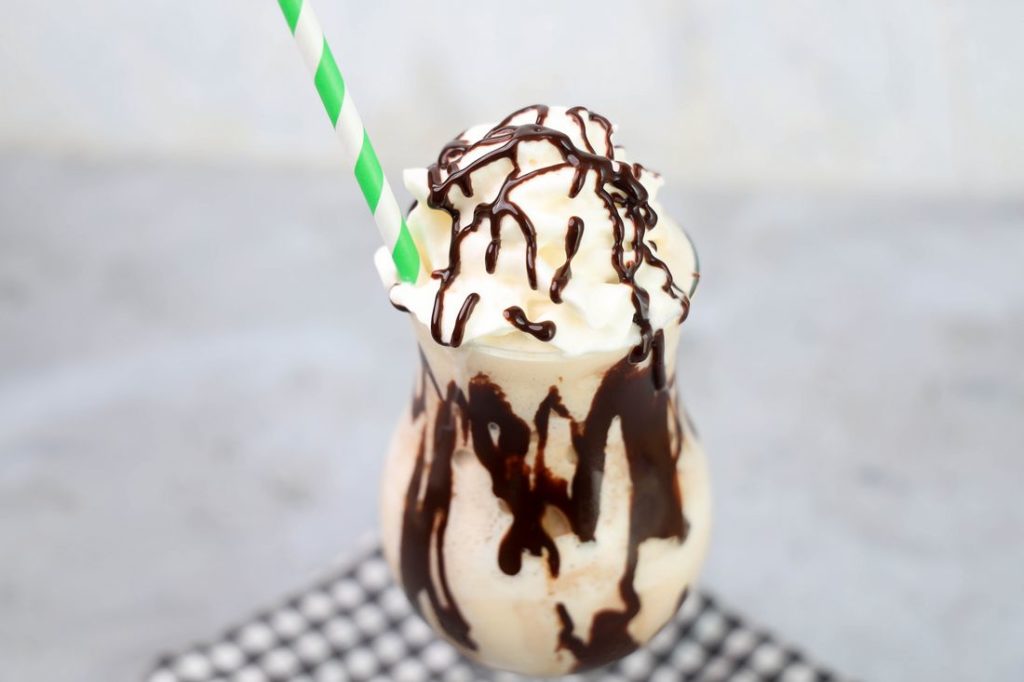 Bailey's Milkshake topped with whipped topping and chocolate syrup on a gray plaid napkin on a concrete backdrop