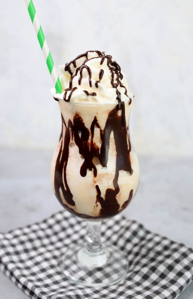 Bailey's Milkshake topped with whipped topping and chocolate syrup on a gray plaid napkin on a concrete backdrop