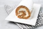 Carrot Cake Roll on a white plate dusted with powdered sugar with a gray plaid napkin and concrete backdrop