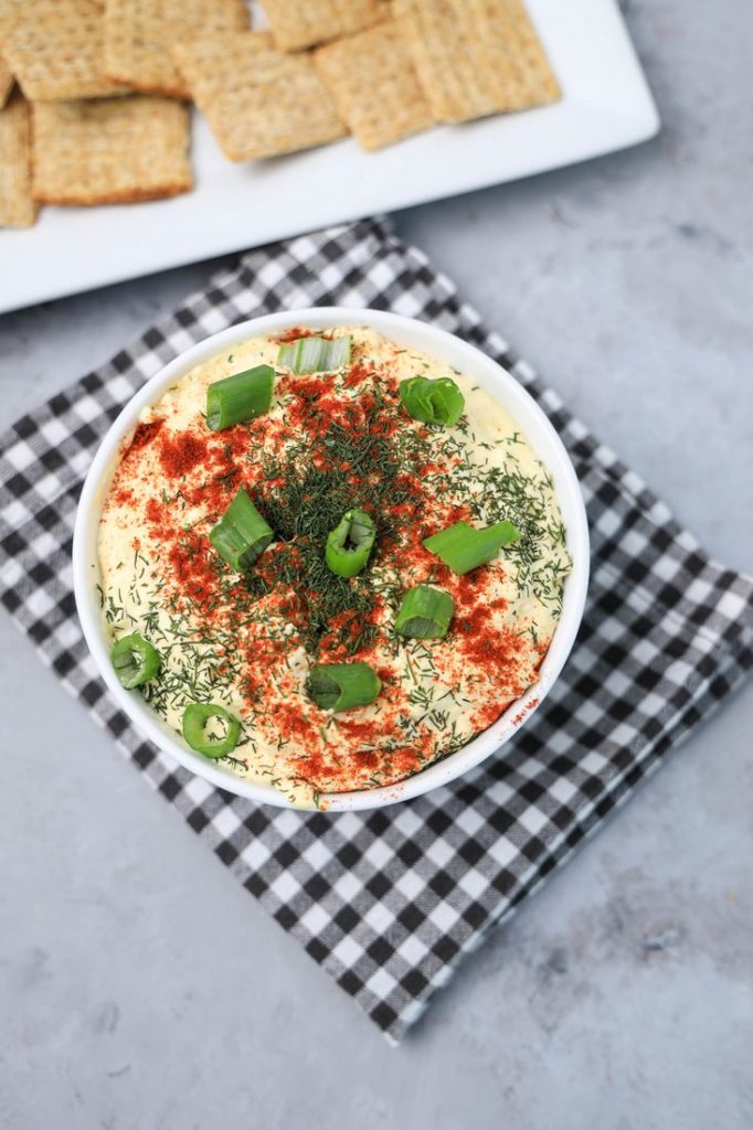 Deviled Eggs Dip in a white bowl on a plaid gray napkin on a concrete backdrop