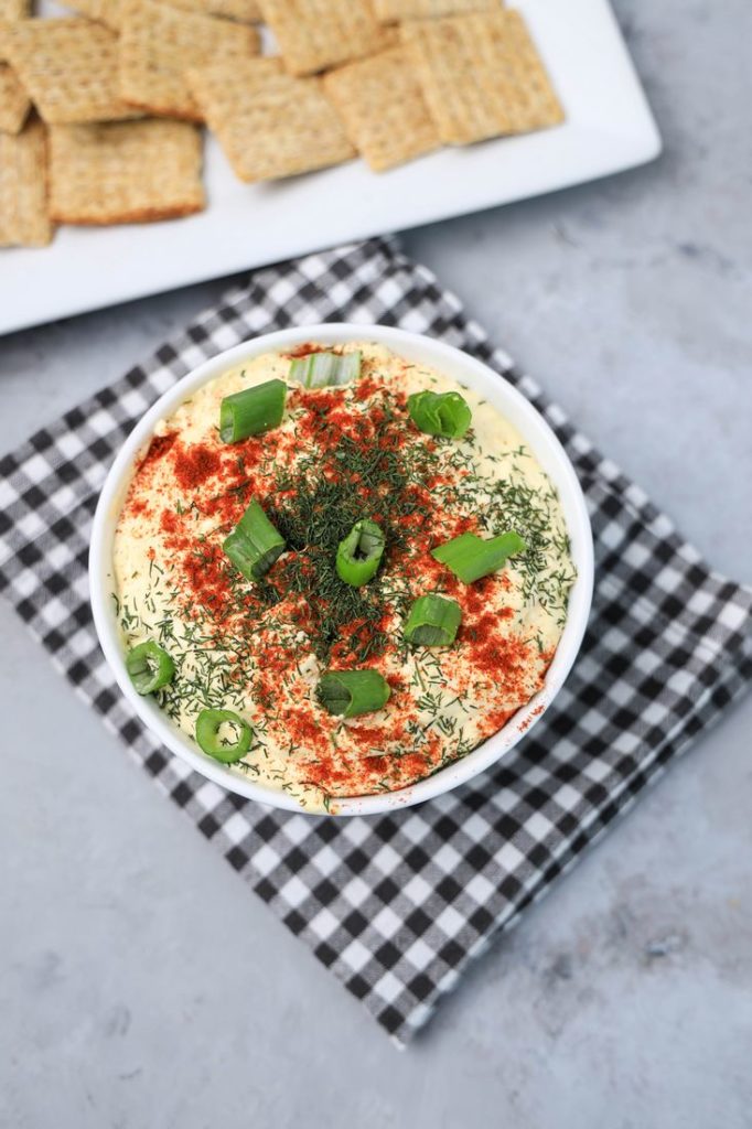 Deviled Eggs Dip in a white bowl on a plaid gray napkin on a concrete backdrop