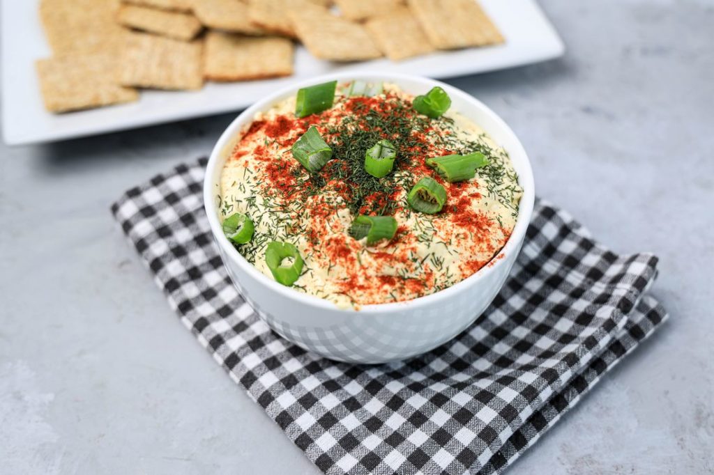 Deviled Eggs Dip in a white bowl on a plaid gray napkin on a concrete backdrop