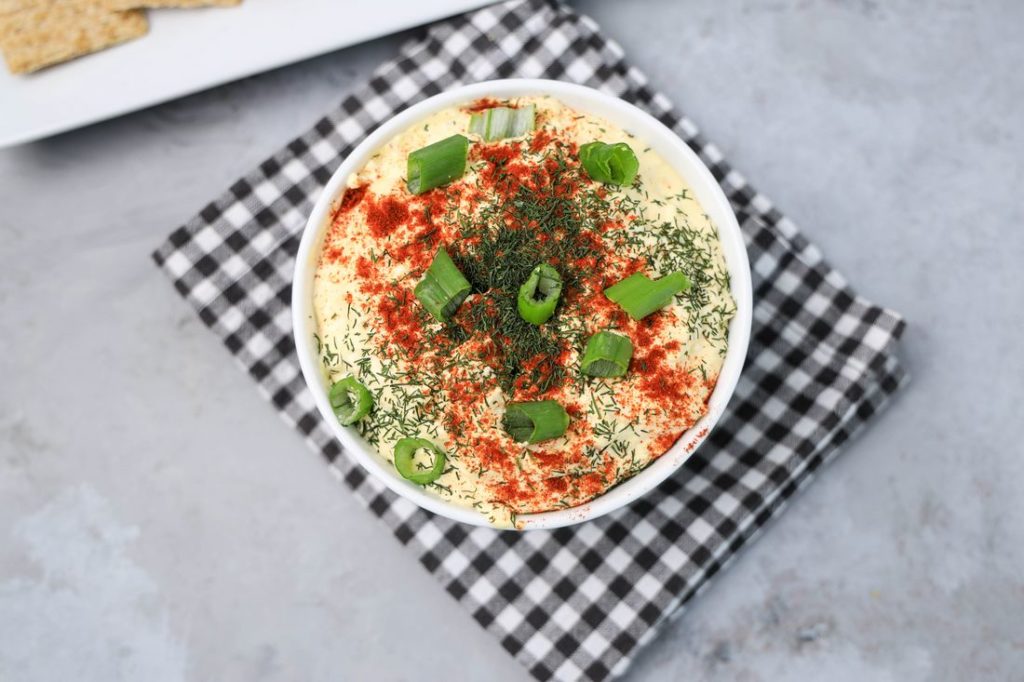 Deviled Eggs Dip in a white bowl on a plaid gray napkin on a concrete backdrop