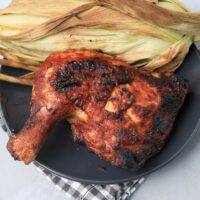 BBQ Picnic Chicken on a gray plate with gray plaid napkin on a concrete backdrop