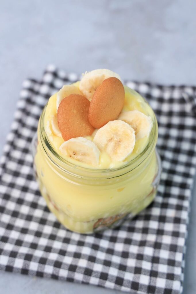 Banana Pudding Jars on a gray plaid napkin on a concrete backdrop