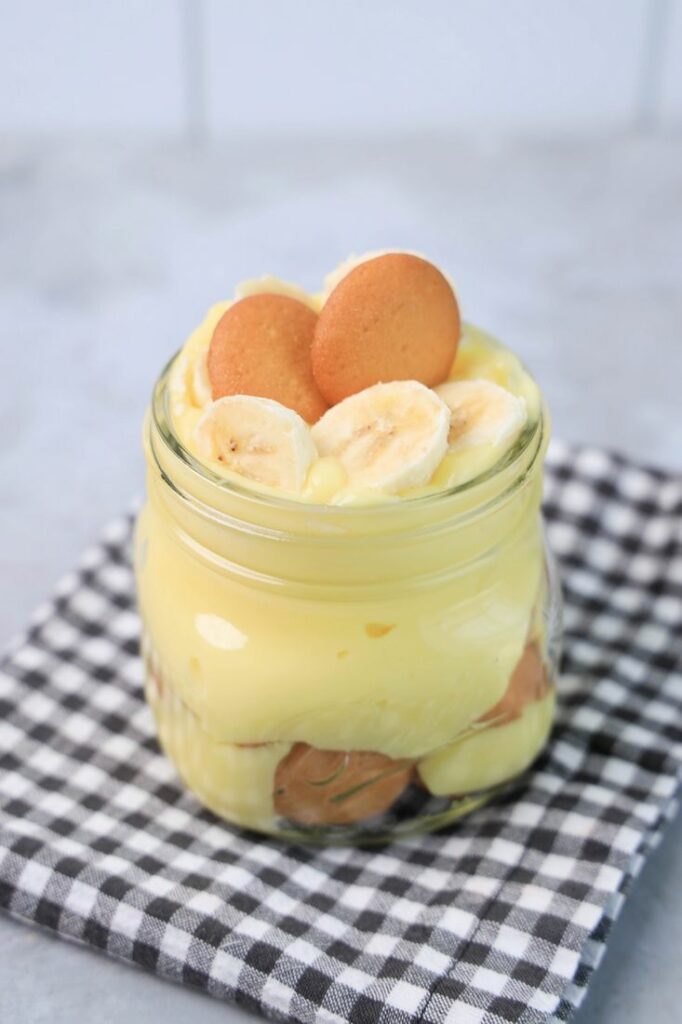 Banana Pudding Jars on a gray plaid napkin on a concrete backdrop