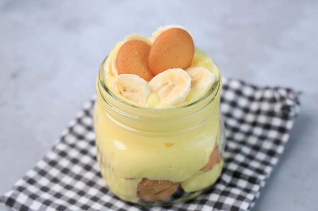 Banana Pudding Jars on a gray plaid napkin on a concrete backdrop