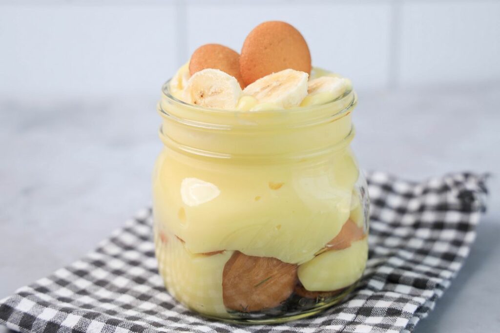 Banana Pudding Jars on a gray plaid napkin on a concrete backdrop