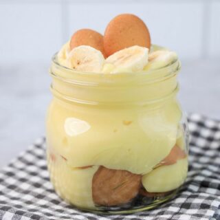 Banana Pudding Jars on a gray plaid napkin on a concrete backdrop