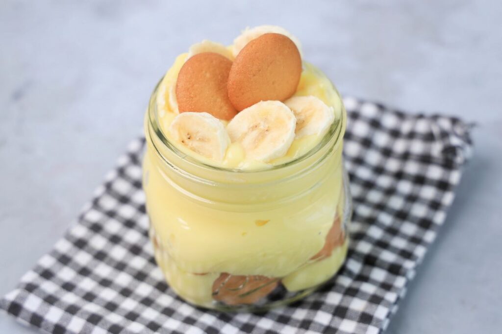 Banana Pudding Jars on a gray plaid napkin on a concrete backdrop