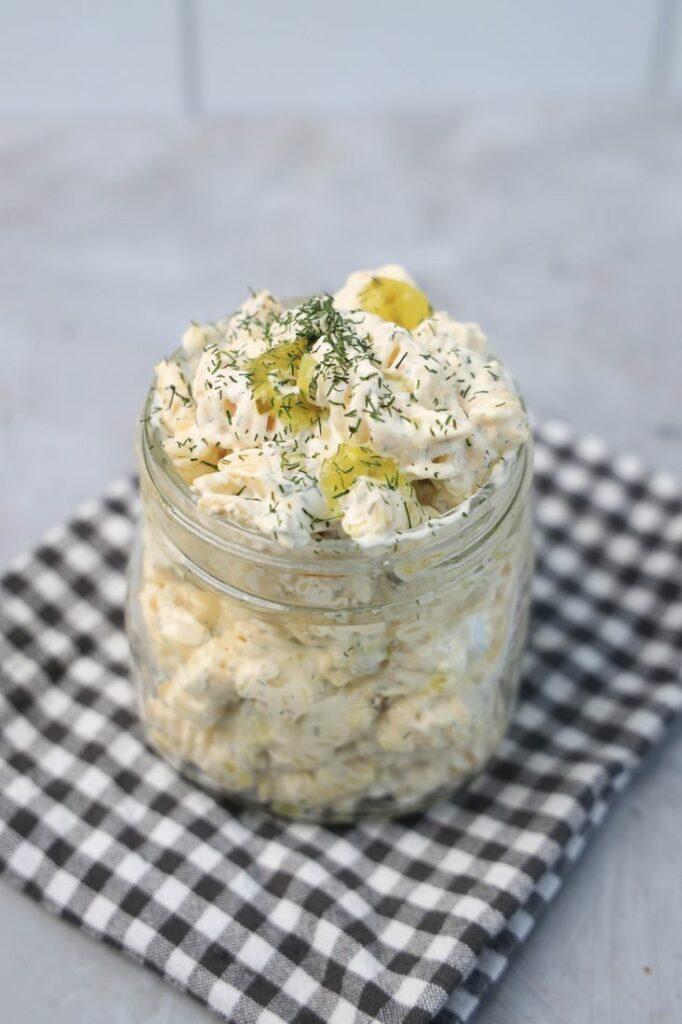 Dill pickle pasta salad in a clear mason jar on a grey plaid napkin on a concrete backdrop