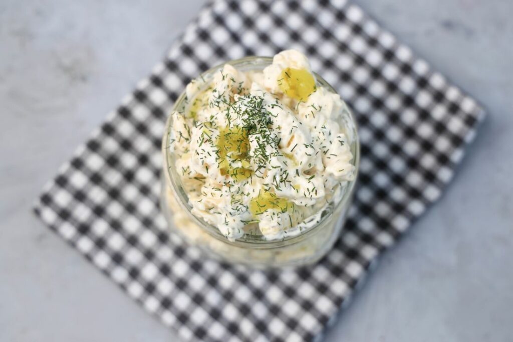 Dill pickle pasta salad in a clear mason jar on a grey plaid napkin on a concrete backdrop