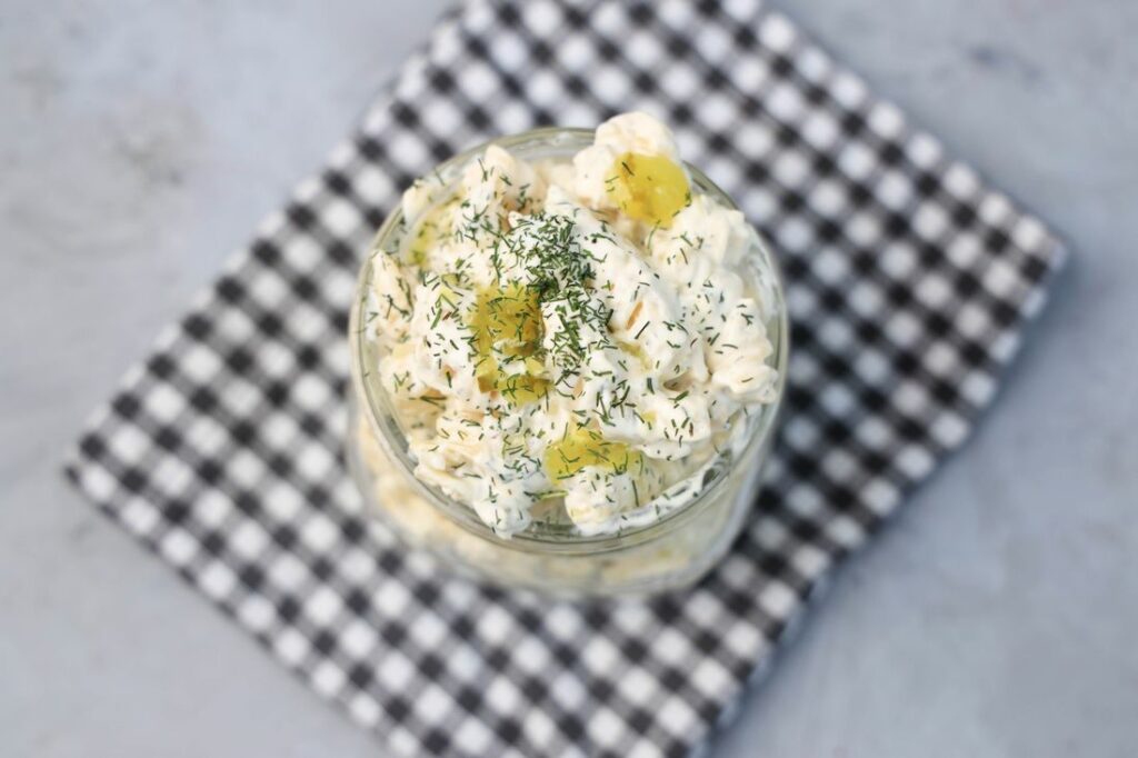 Dill pickle pasta salad in a clear mason jar on a grey plaid napkin on a concrete backdrop