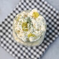 Dill pickle pasta salad in a clear mason jar on a grey plaid napkin on a concrete backdrop