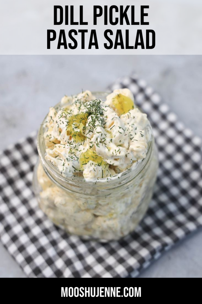 Dill pickle pasta salad in a clear mason jar on a grey plaid napkin on a concrete backdrop