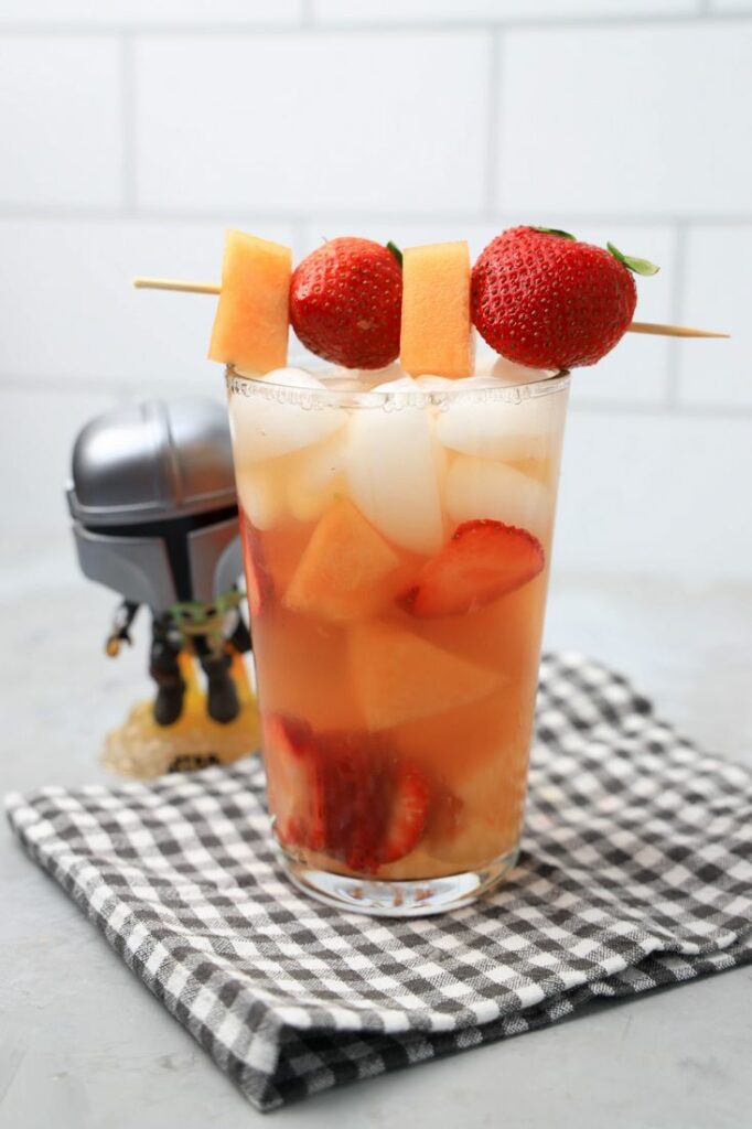 Tatooine sunset drink with cantaloupe and strawberries in a glass on a gray plaid napkin on a concrete backdrop.