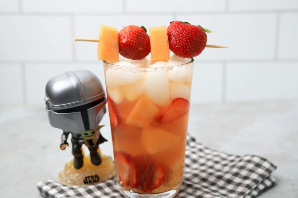 Tatooine sunset drink with cantaloupe and strawberries in a glass on a gray plaid napkin on a concrete backdrop.