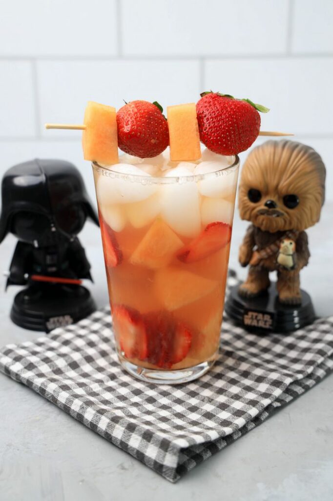 Tatooine sunset drink with cantaloupe and strawberries in a glass on a gray plaid napkin on a concrete backdrop.