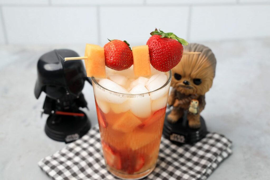 Tatooine sunset drink with cantaloupe and strawberries in a glass on a gray plaid napkin on a concrete backdrop.