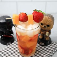 Tatooine sunset drink with cantaloupe and strawberries in a glass on a gray plaid napkin on a concrete backdrop.