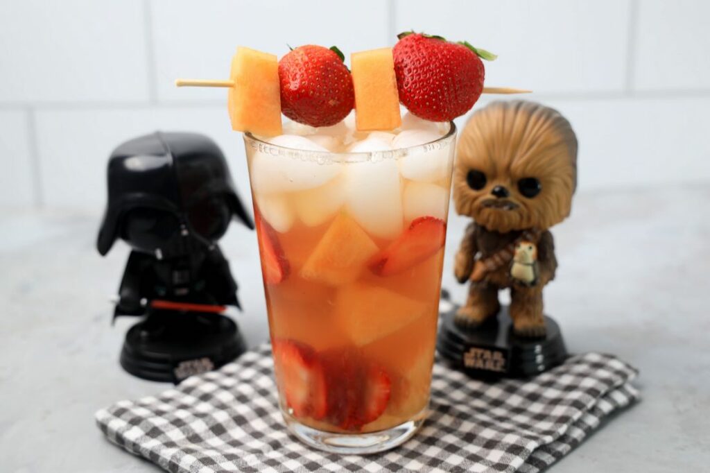 Tatooine sunset drink with cantaloupe and strawberries in a glass on a gray plaid napkin on a concrete backdrop.