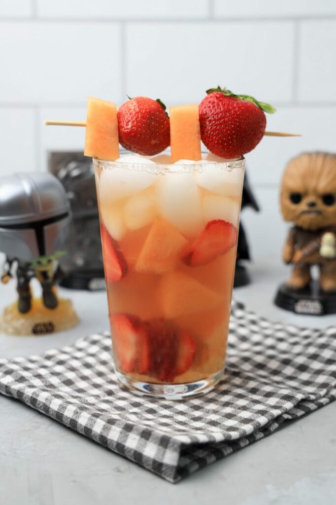 Tatooine sunset drink with cantaloupe and strawberries in a glass on a gray plaid napkin on a concrete backdrop.