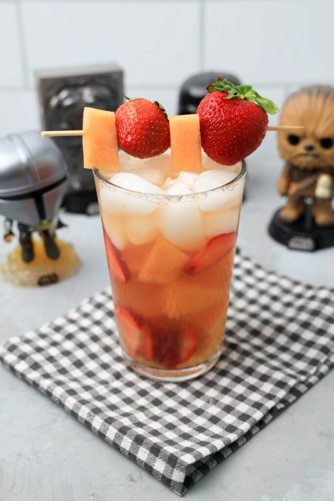 Tatooine sunset drink with cantaloupe and strawberries in a glass on a gray plaid napkin on a concrete backdrop.