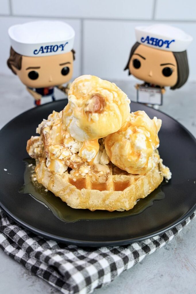 Butterscotch ice cream on a waffle on a gray plate on a grey plaid napkin on a concrete backdrop with stranger things funko pops