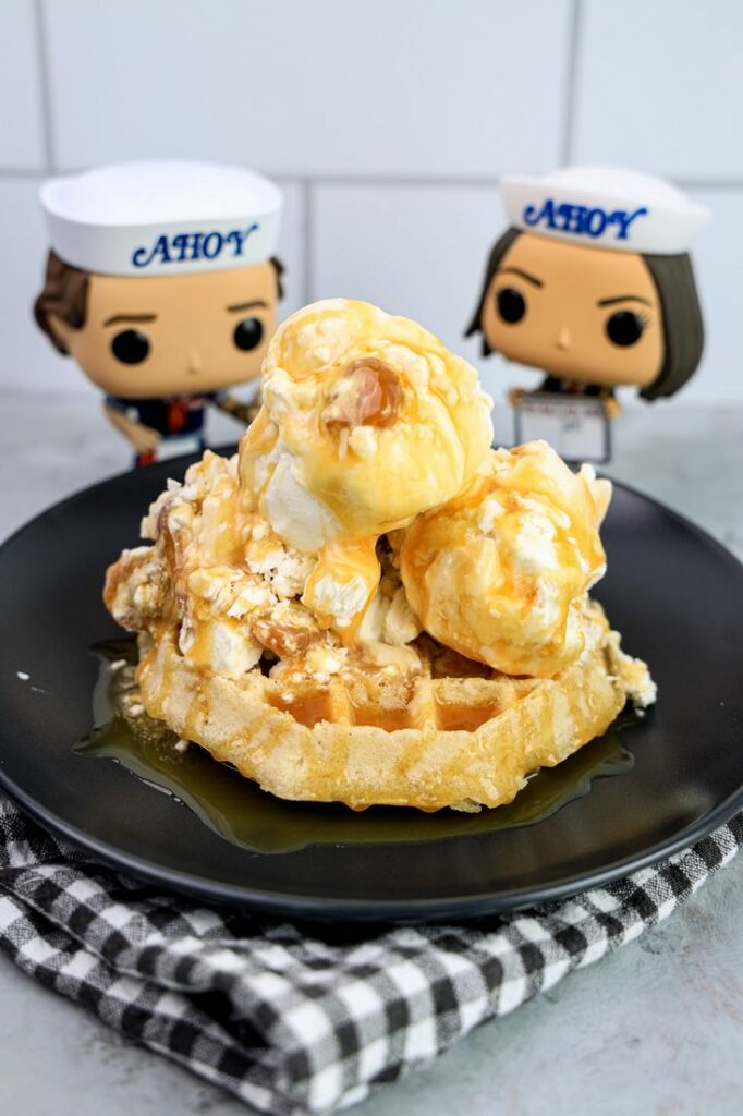 Butterscotch ice cream on a waffle on a gray plate on a grey plaid napkin on a concrete backdrop with stranger things funko pops