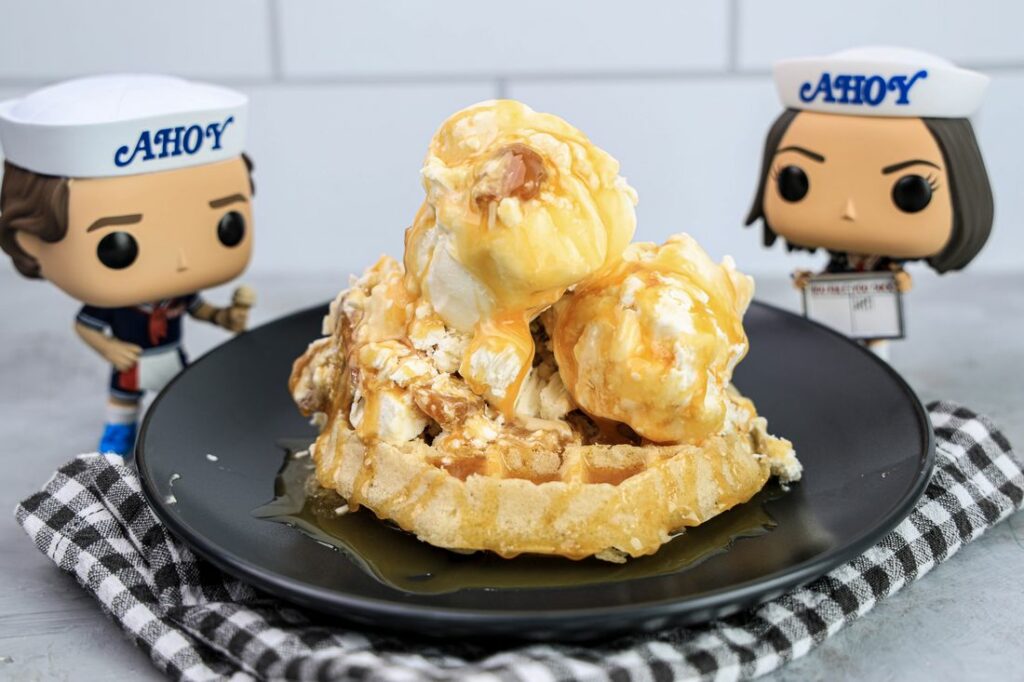 Butterscotch ice cream on a waffle on a gray plate on a grey plaid napkin on a concrete backdrop with stranger things funko pops