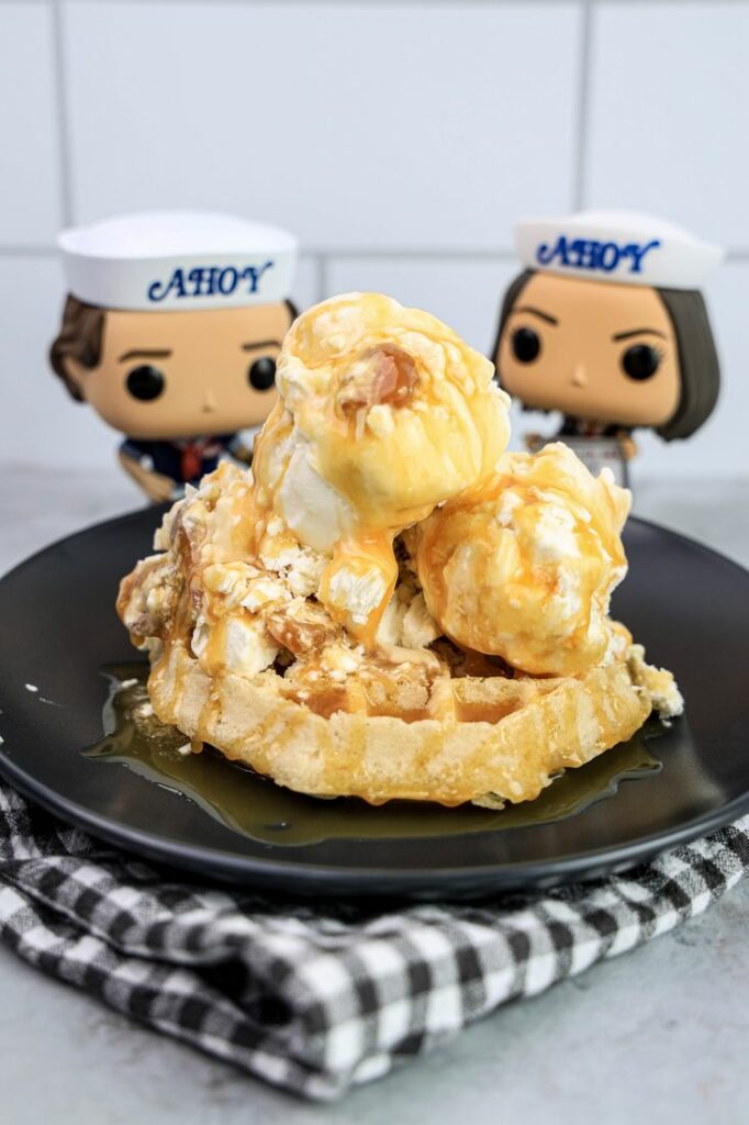 Butterscotch ice cream on a waffle on a gray plate on a grey plaid napkin on a concrete backdrop with stranger things funko pops