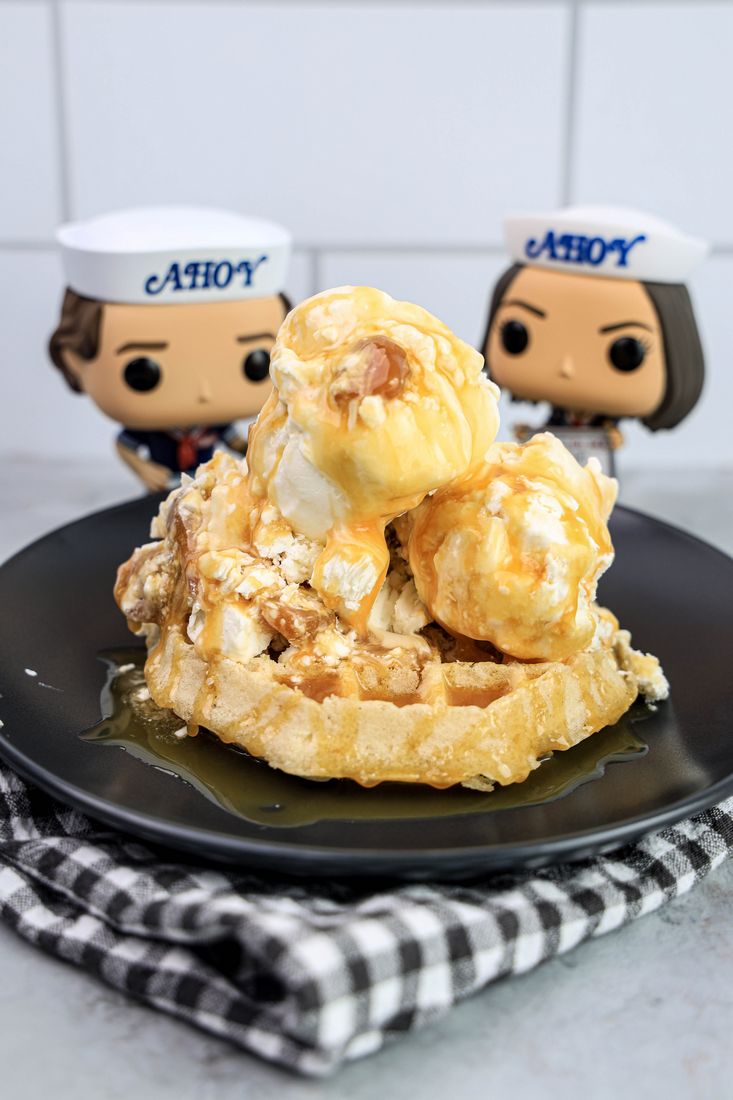 Butterscotch ice cream on a waffle on a gray plate on a grey plaid napkin on a concrete backdrop with stranger things funko pops