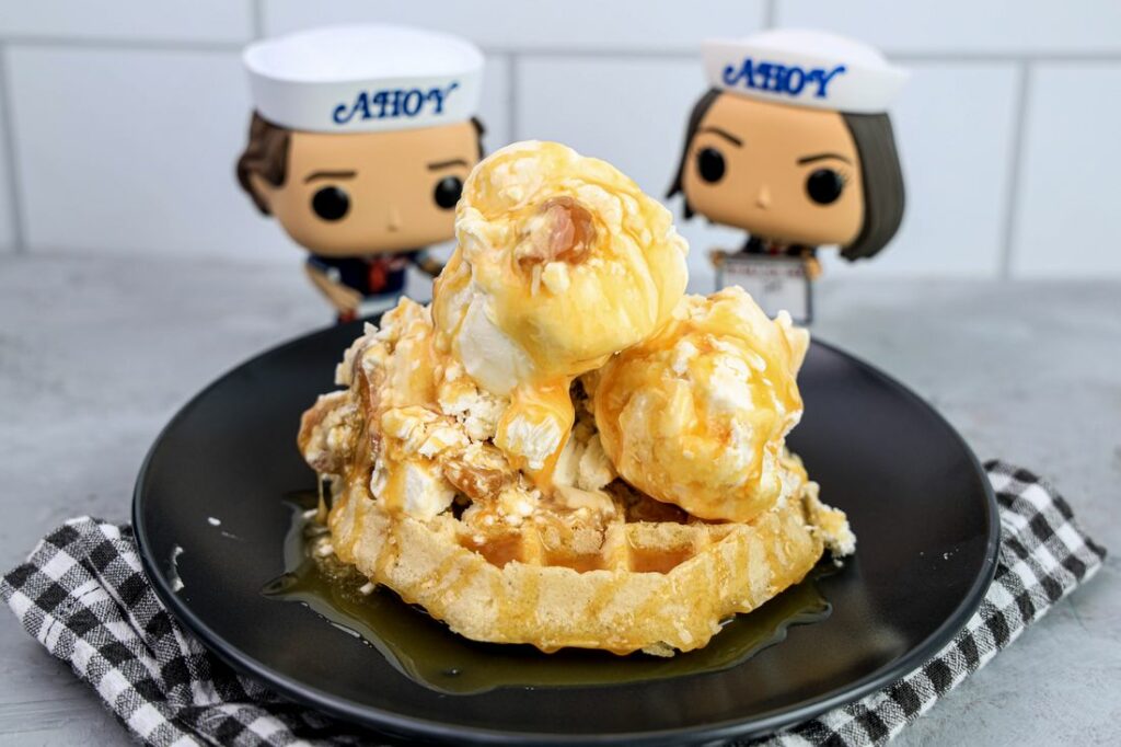 Butterscotch ice cream on a waffle on a gray plate on a grey plaid napkin on a concrete backdrop with stranger things funko pops