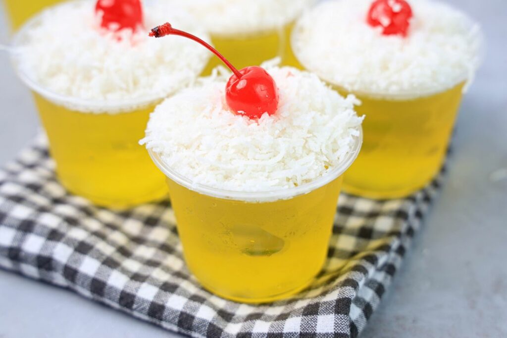 Pina colada jello shot topped with coconut and a cherry.