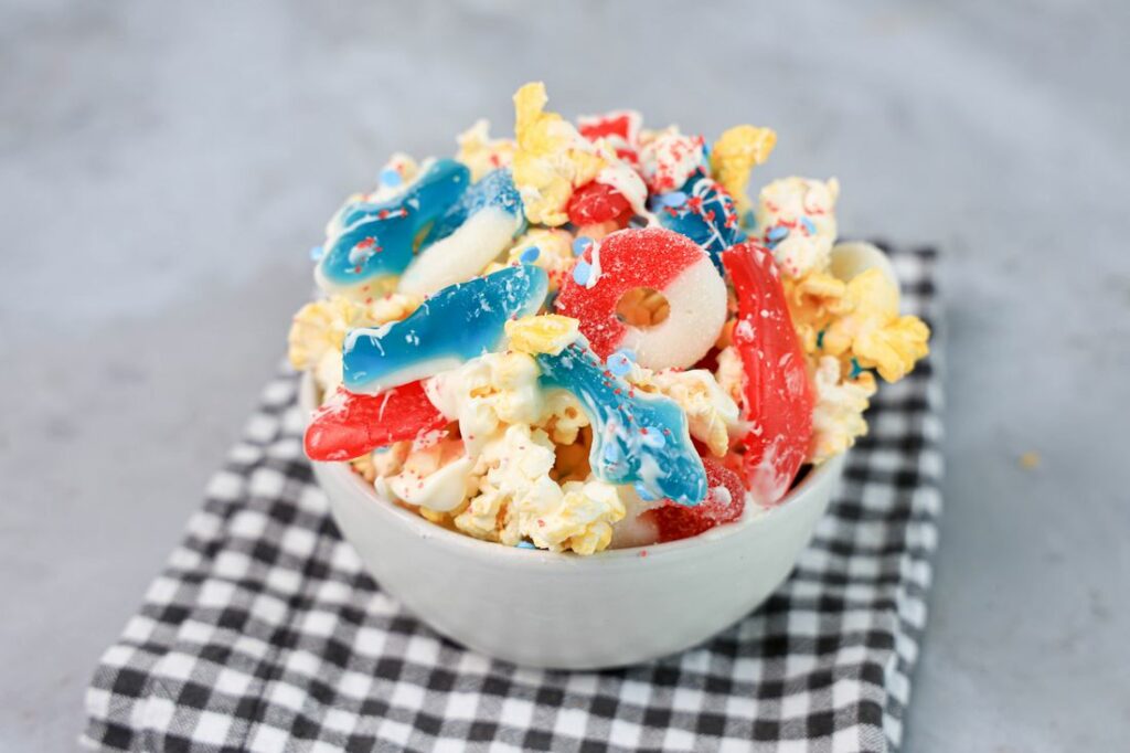 Shark week popcorn with shark gummies and red swedish fish in a white bowl on a gray plaid napkin on a concrete backdrop