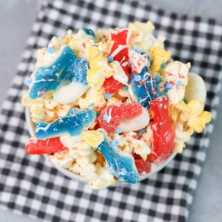 Shark week popcorn with shark gummies and red swedish fish in a white bowl on a gray plaid napkin on a concrete backdrop