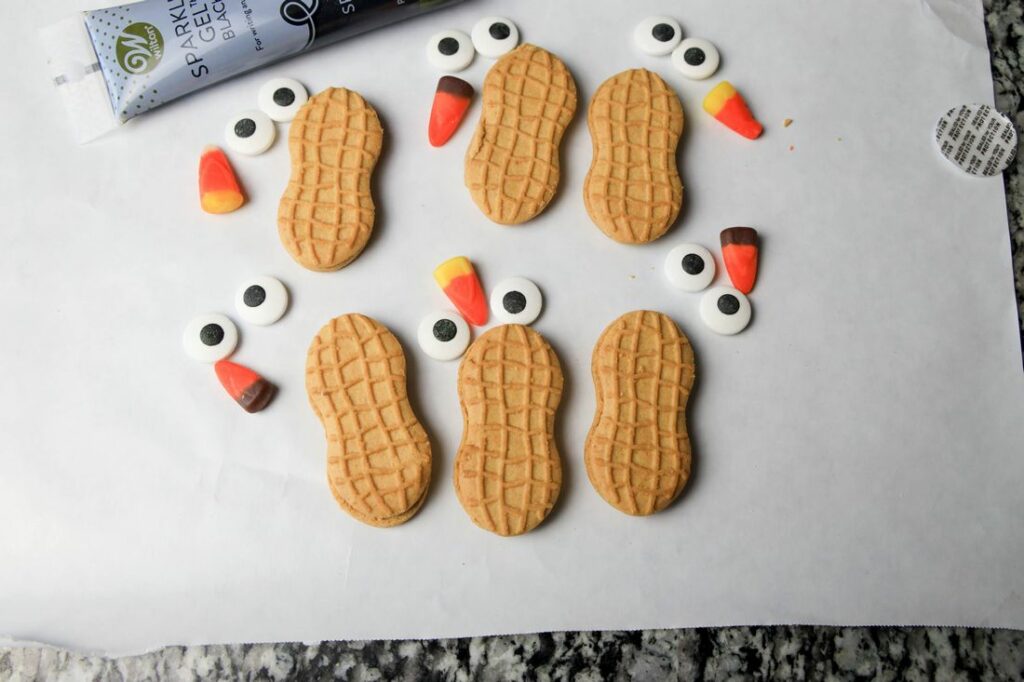 Nutter butter cookies, candy corn, candy eyes, and black sparkle gel on parchment paper.