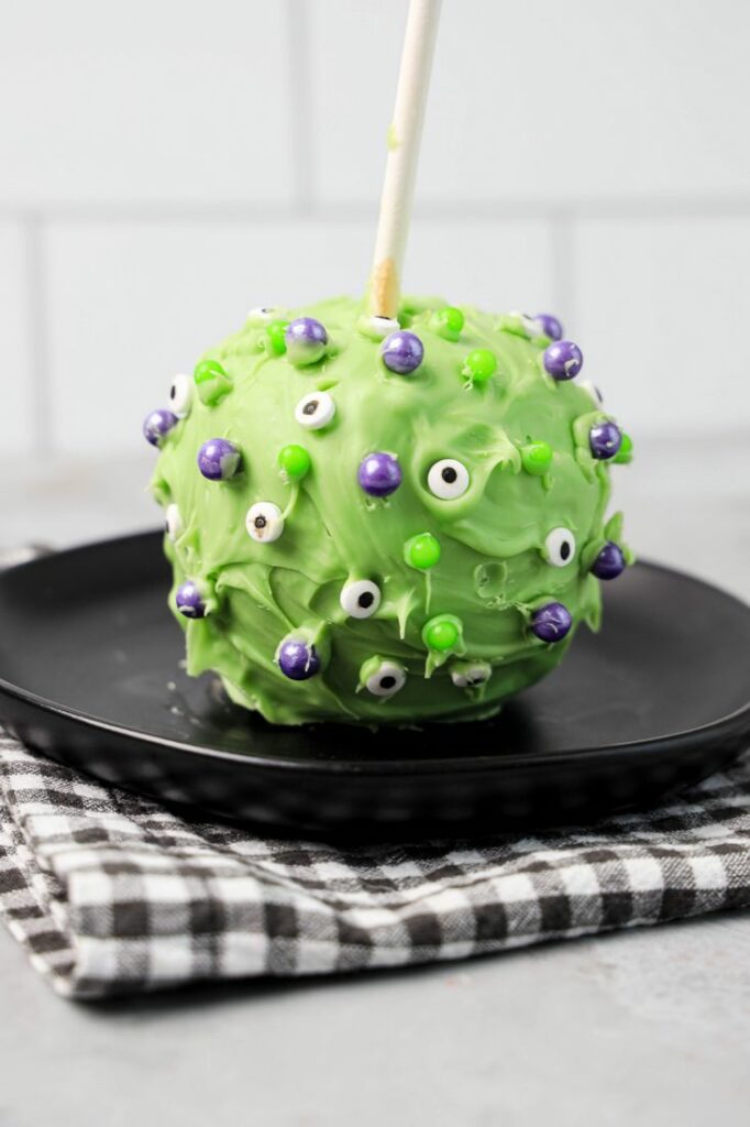 Hocus Pocus Candied Apple on a black plate with a gray plaid napkin on a concrete backdrop