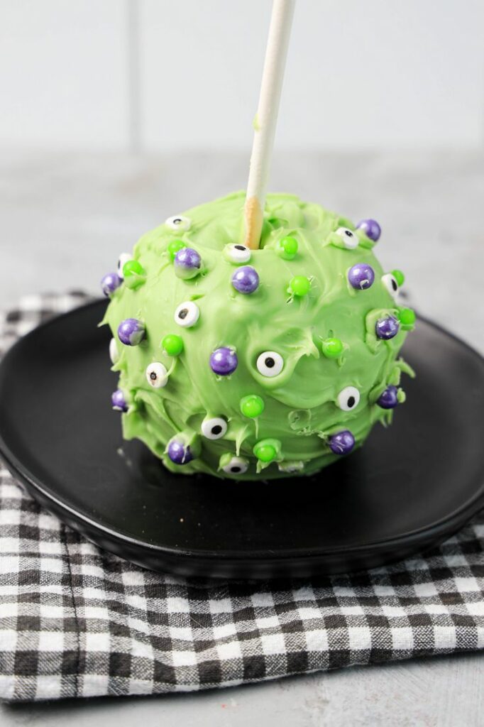 Hocus Pocus Candied Apple on a black plate with a gray plaid napkin on a concrete backdrop