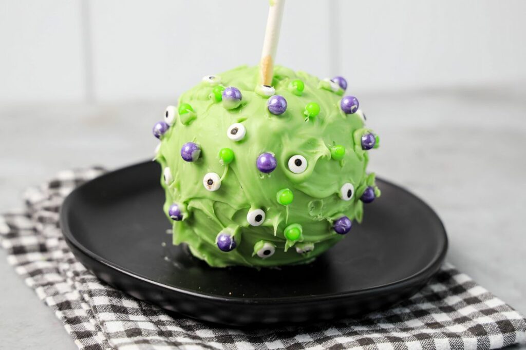 Hocus Pocus Candied Apple on a black plate with a gray plaid napkin on a concrete backdrop