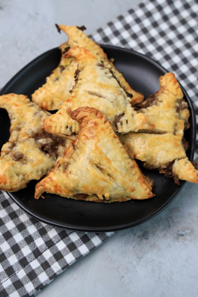 Hocus Pocus Savory Witch Hat Pies on a black plate with a gray plaid napkin on a concrete backdrop