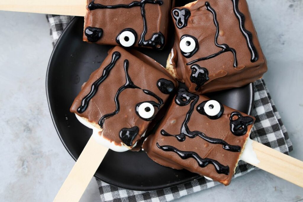 Hocus Pocus S'mores Pops on a black plate with a gray plaid napkin on a faux concrete backdrop