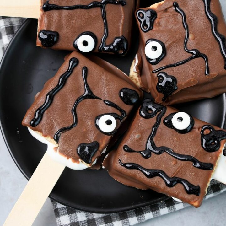 Hocus Pocus Book Of Spells S'mores Pops on a black plate with a gray plaid napkin on a faux concrete backdrop