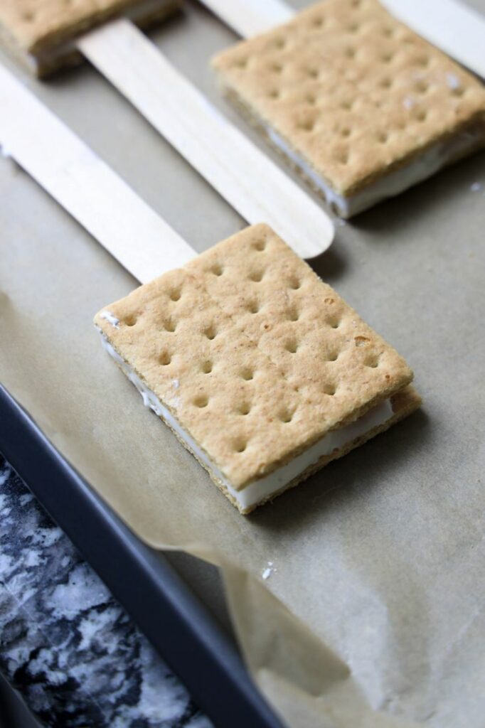 Graham cracker sandwich with marshmallow fluff and a pop stick.