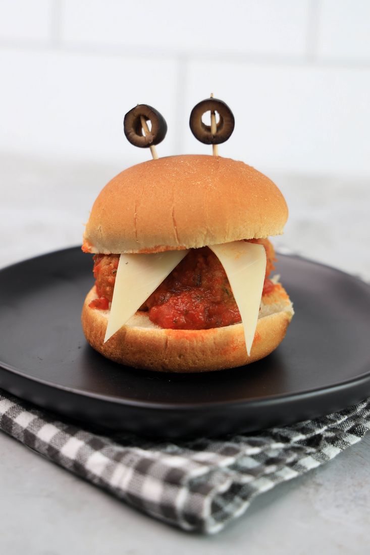 Monster meatball slider with cheese as teeth and meatball in the middle. Toothpicks with black olives as eyes.
