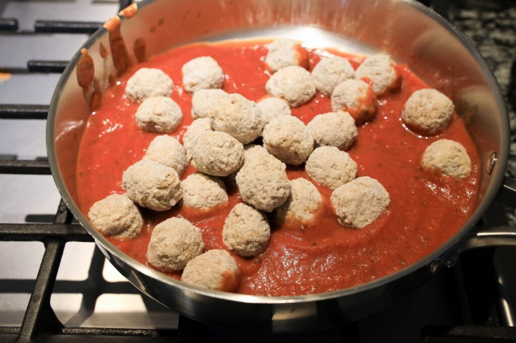 Frozen meatballs in a deep skillet with spaghetti sauce.